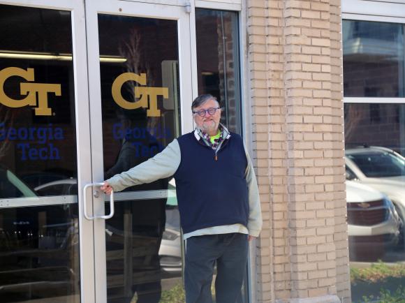 A man standing in front of glass double doors with the Georgia Tech logo.