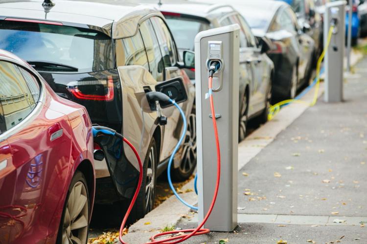 Row of electric vehicles parked on a street and charging from charging poles