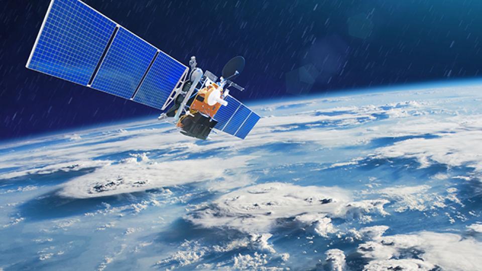 Satellite with large blue solar panels orbiting above Earth, showing cloud formations and the planet's curvature against a dark space background